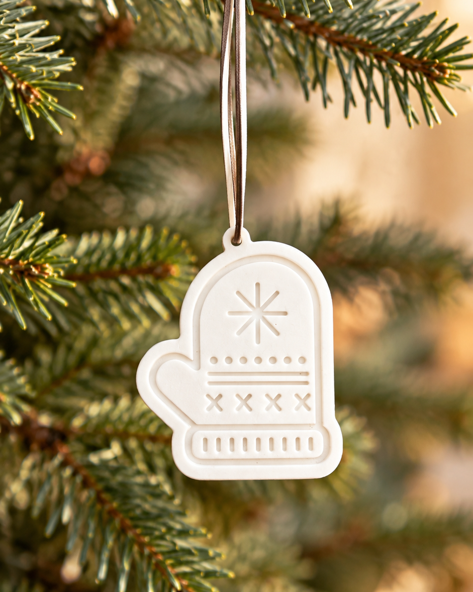 Petite suspension de Noël en forme de moufle blanche, réalisée à la main en résine époxy et suspendue à une branche de sapin.
