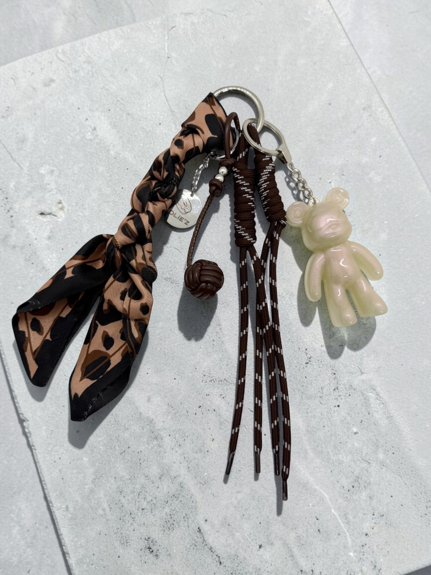 Grigri de sac Lolie’z avec Teddy’z nacré en résine époxy, foulard imprimé léopard, cordons marron et breloque chocolat, assemblé à la main en France.