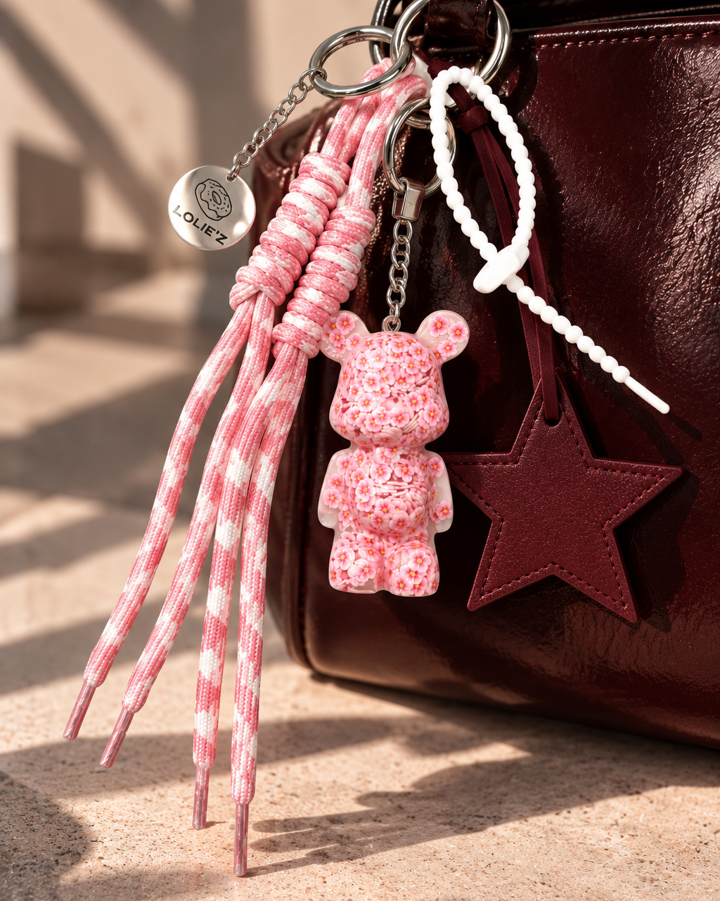 Grigri de sac Lolie’z avec Teddy’z rose fleuri en résine époxy, grande étoile bordeaux, cordons roses et médaille gravée, assemblé à la main en France.