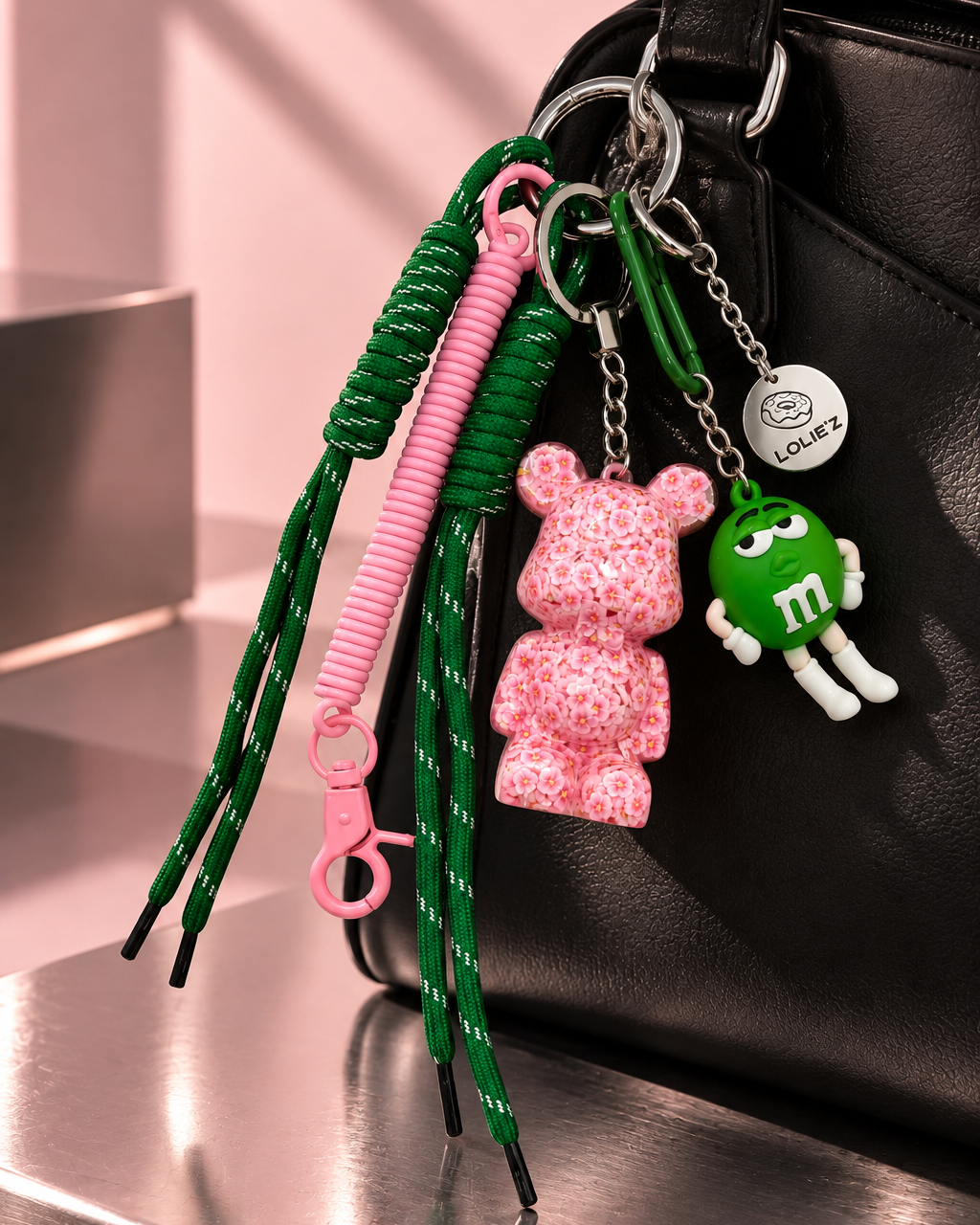 Grigri de sac Lolie’z rose et vert avec Teddy’z fleuri en résine époxy, cordons verts, mousqueton rose et breloque bonbon, assemblé à la main en France.