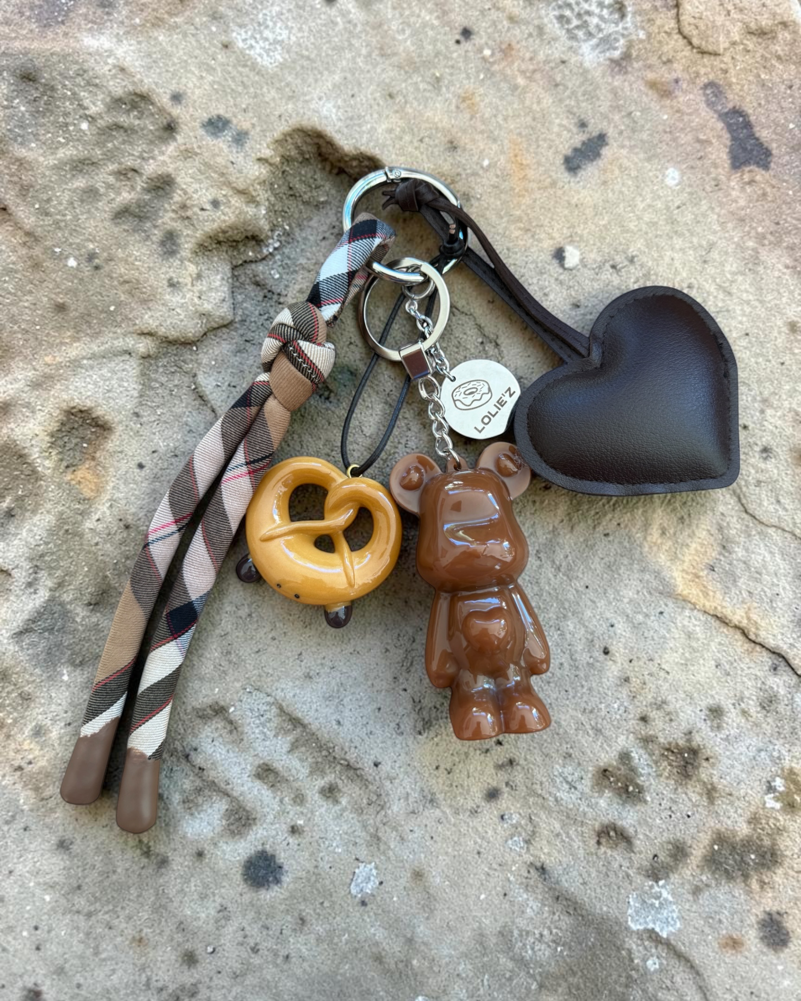 kMarley Crazy Pretzel, grigri de sac chocolat avec bretzel, grand cœur marron, ruban tartan et médaille Lolie’z.