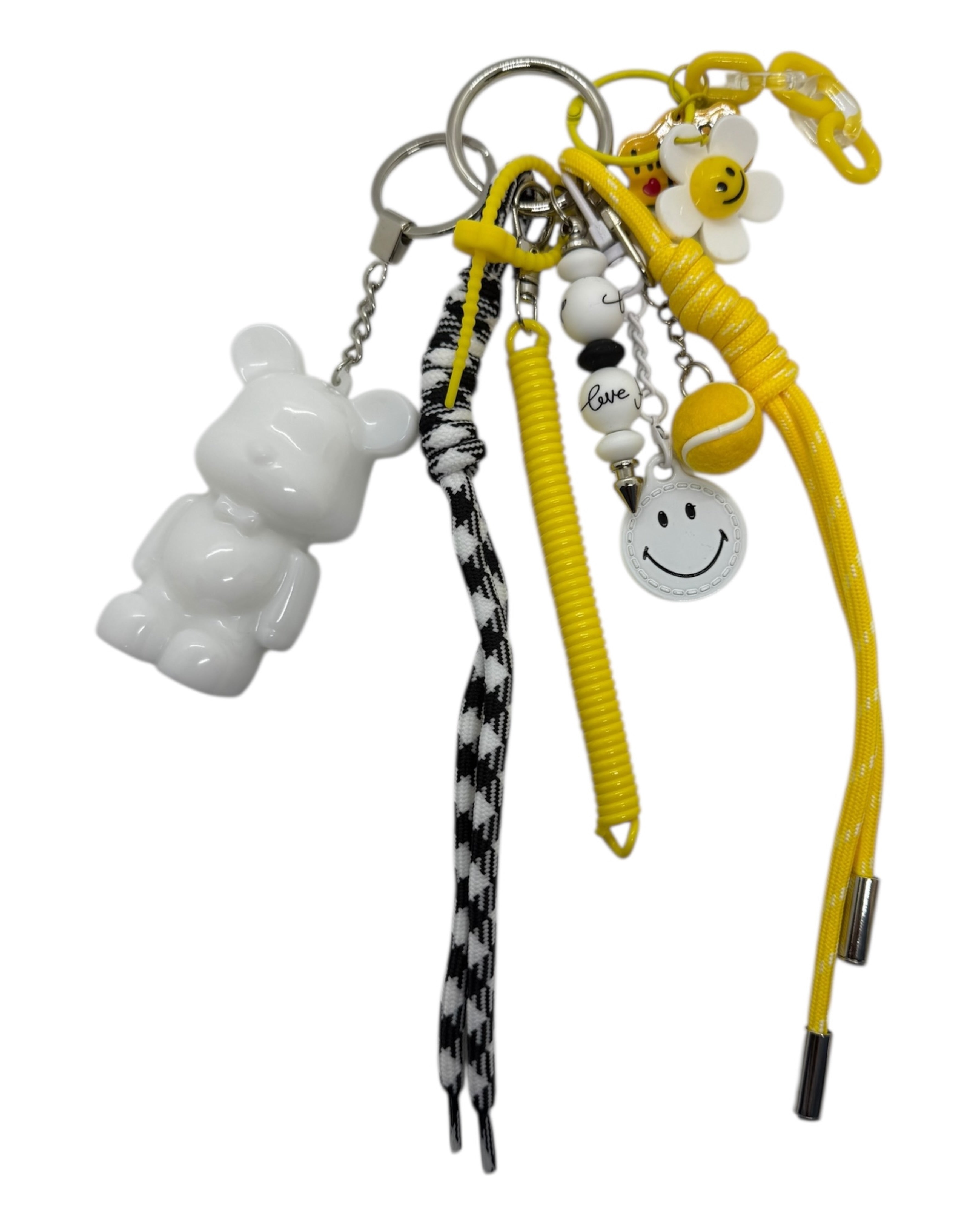 Grigri Pop Smile avec Teddy’z blanc, cordons jaune et noir à motifs, fleur et smiley, création faite main pleine de bonne humeur.