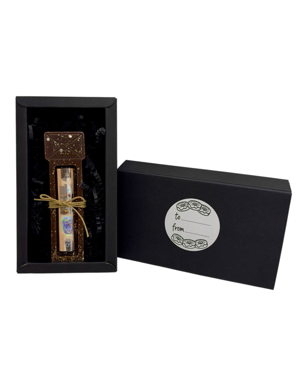 Support à billet Love Letter avec enveloppe chocolat à cœur en relief, paillettes dorées, billet roulé et ficelle naturelle, dans son coffret cadeau noir avec étiquette To From sur fond blanc.