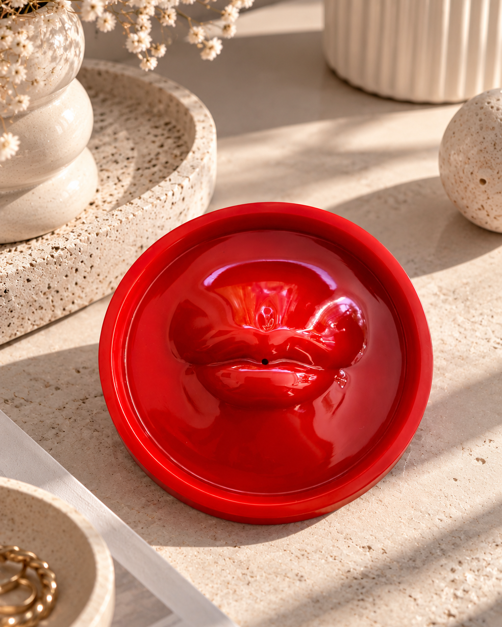 Porte-encens Bisou Bisou en résine époxy rouge brillant, orné d'une bouche en relief, posé sur une surface en pierre beige dans une ambiance design contemporaine aux tons naturels.