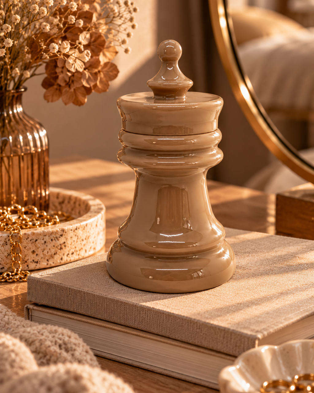 Boîte décorative en résine époxy beige taupe brillant, en forme de pièce d’échecs avec couvercle, posée sur une coiffeuse en marbre clair près d’une lampe, d’une bougie allumée et d’un miroir doré, dans une chambre élégante et chaleureuse.
