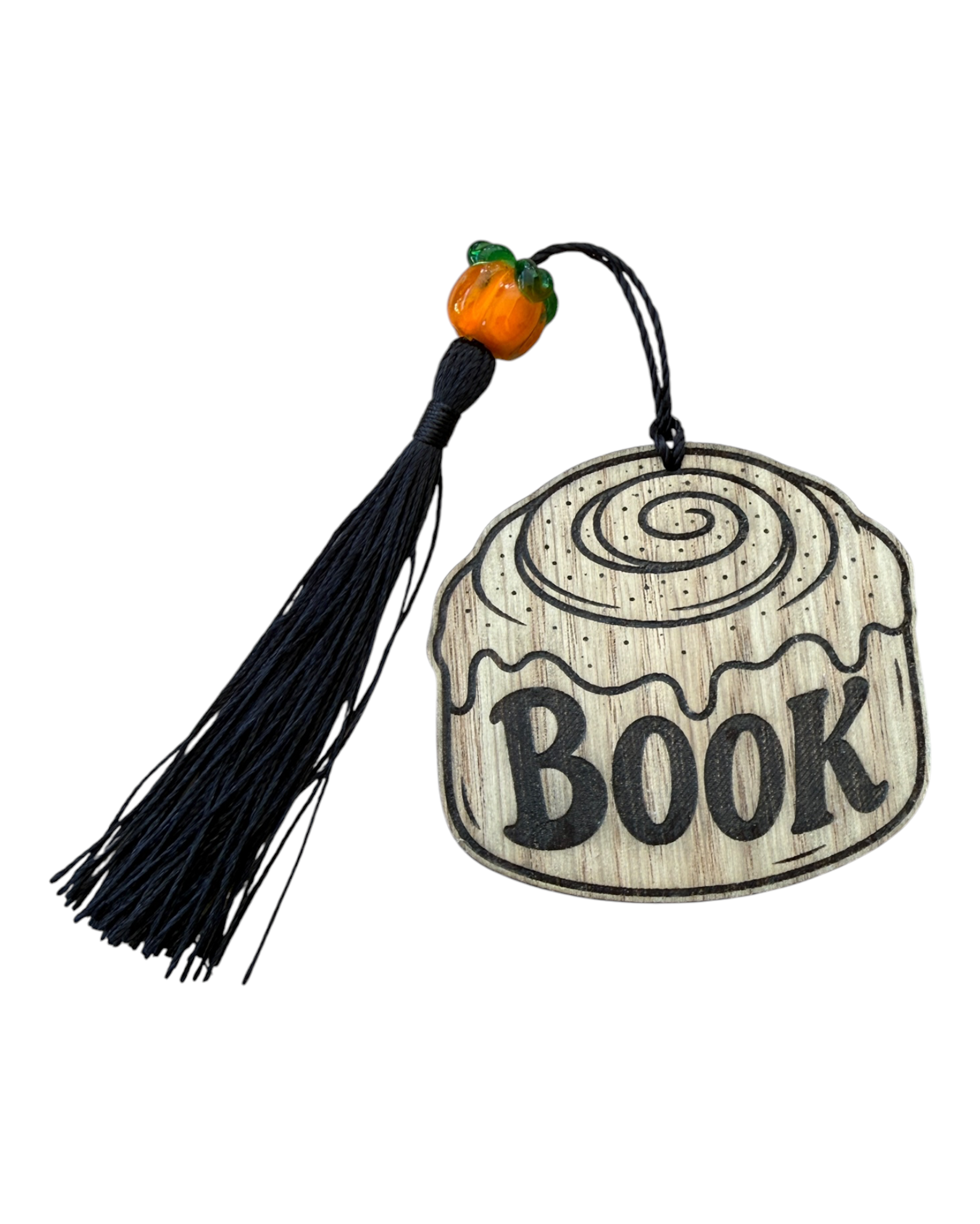 Bookmark en bois en forme de cinnamon roll gravé BOOK, accompagné d’un pompon noir et d’une petite citrouille.