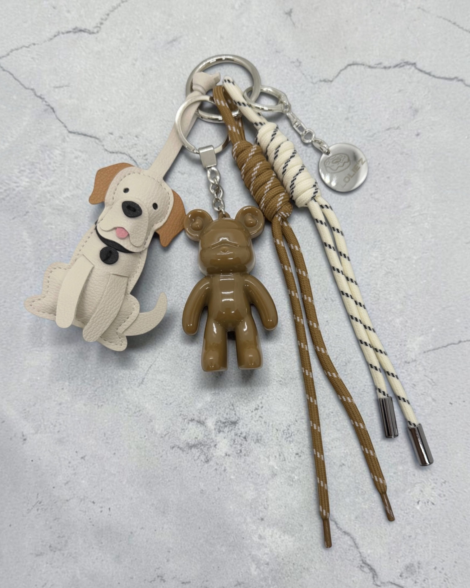 Grigri de sac Lolie’z aux tons beige et camel avec Teddy’z en résine époxy, breloque chien et cordons crème et marron, assemblé à la main en France.