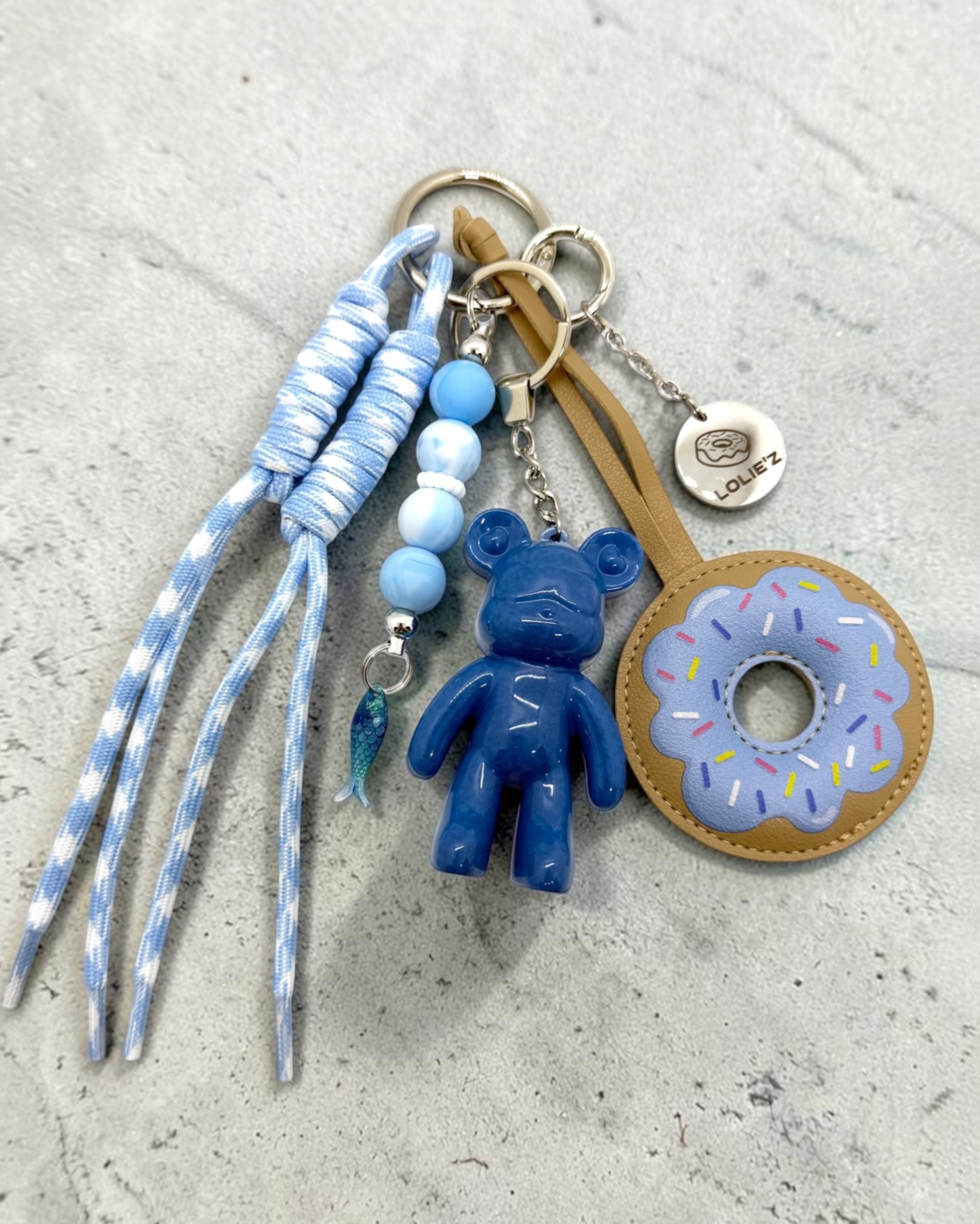 Grigri de sac Lolie’z bleu avec Teddy’z en résine époxy, donut, cordons bleu et blanc, perles et breloque poisson, assemblé à la main en France.
