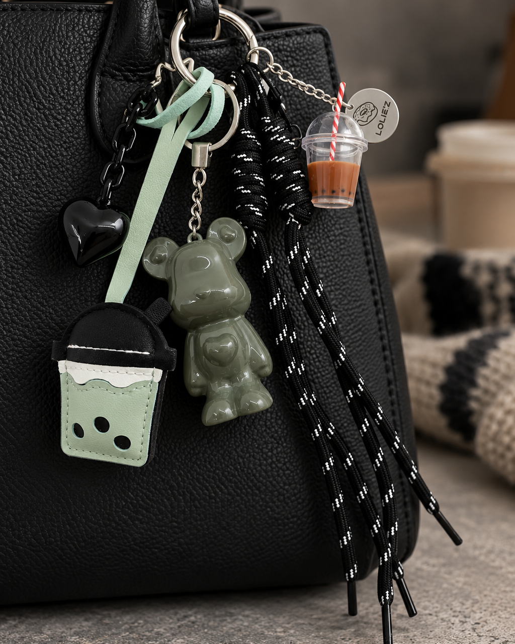 Grigri Marley Bubble Trouble vert kaki brillant accroché à un sac noir, avec cœur noir, accessoires bubble tea vert menthe et cordons noirs à motifs blancs.