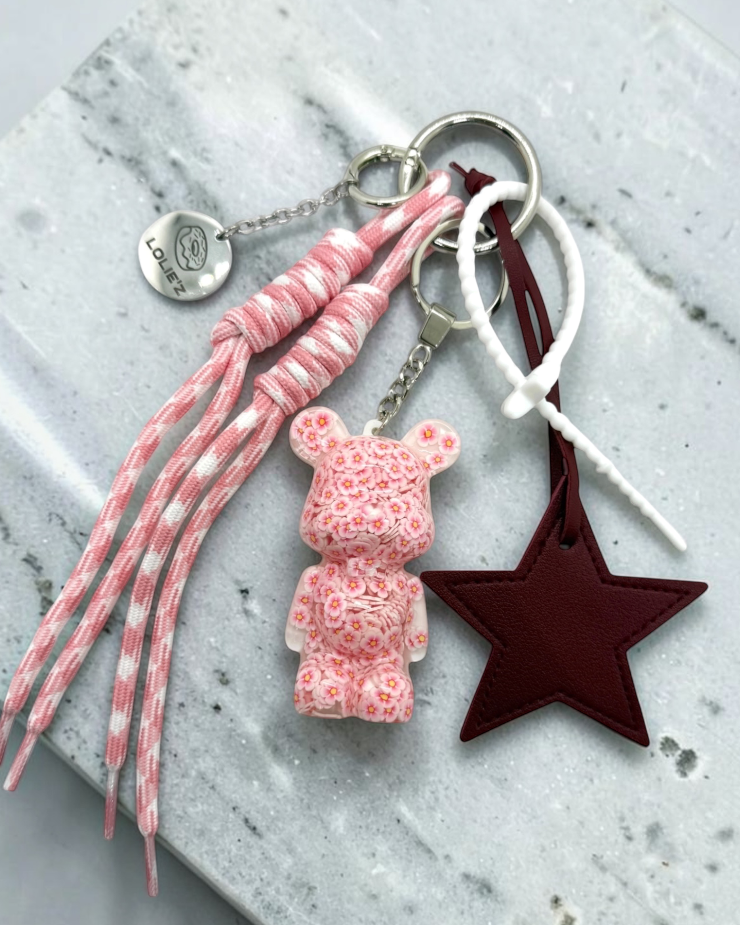 Grigri de sac Lolie’z avec Teddy’z rose fleuri en résine époxy, grande étoile bordeaux, cordons roses et médaille gravée, assemblé à la main en France.