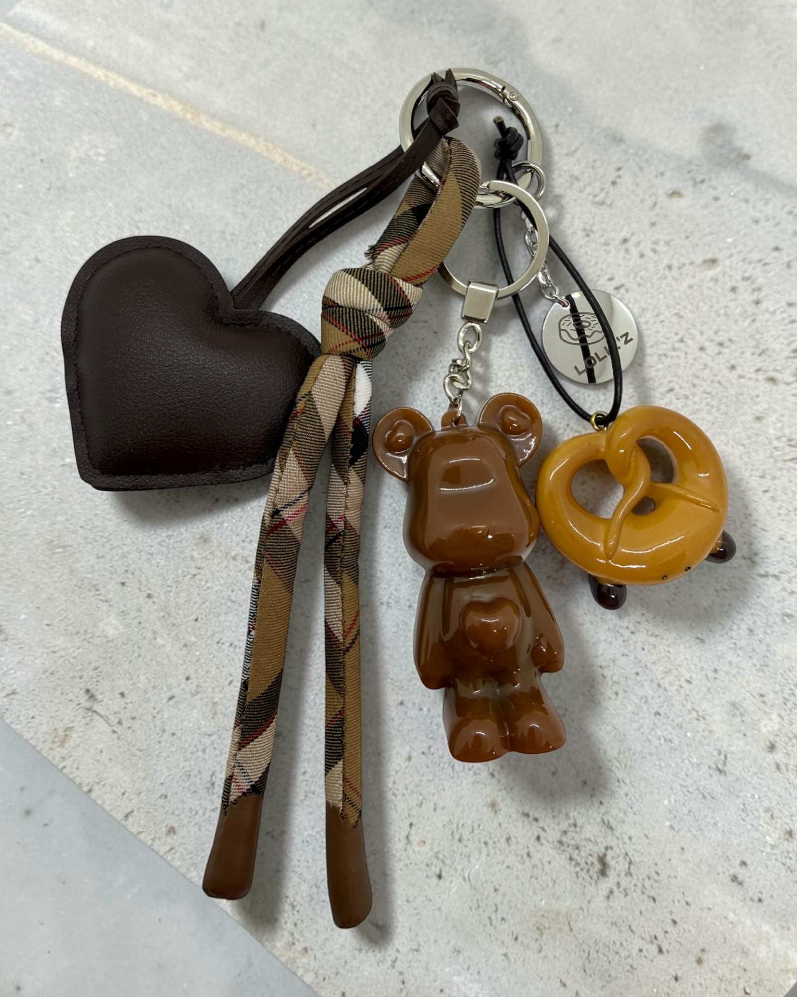 Marley Crazy Pretzel, grigri de sac chocolat avec bretzel, grand cœur marron, ruban tartan et médaille Lolie’z.