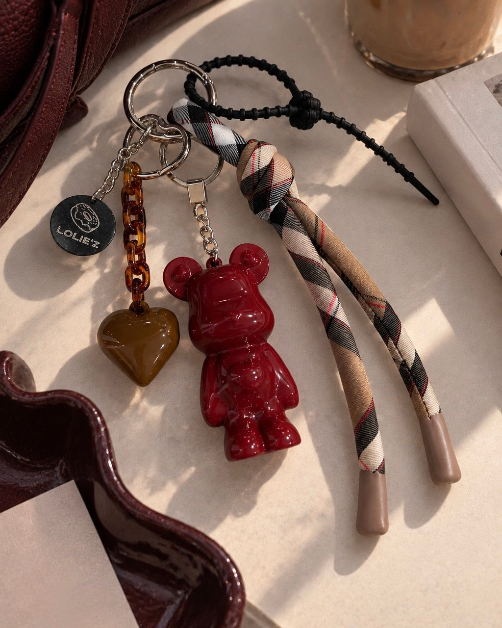 Grigri de sac Marley Sweet Tartan avec Marley bordeaux glossy, cœur choco, chaîne caramel et long ruban tartan.