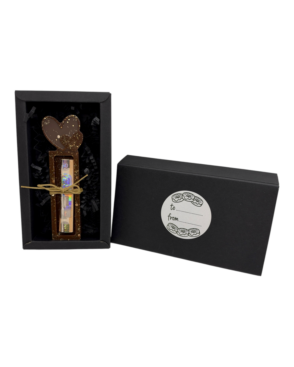 Support à billet Sweet Heart avec deux cœurs chocolat pailletés, billet roulé et nœud en ficelle naturelle, dans son coffret cadeau noir avec étiquette To From sur fond blanc.