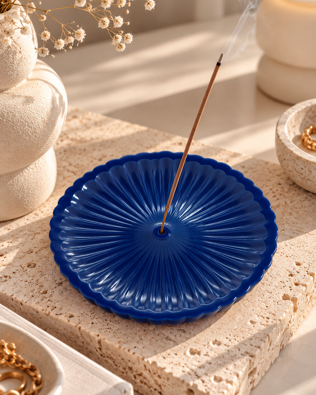 Porte-encens Nami en résine époxy bleu marine brillant, aux reliefs ondulés, accueillant un bâton d’encens fumant sur un socle en travertin beige, dans une ambiance zen et contemporaine.