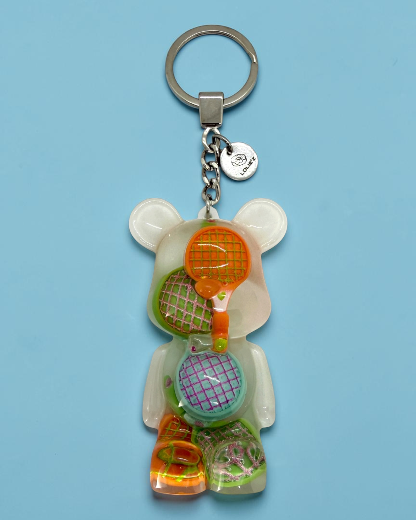 Teddy’z Match Point, porte-clés ours en résine époxy fait main avec plusieurs raquettes de tennis colorées dans son corps transparent.