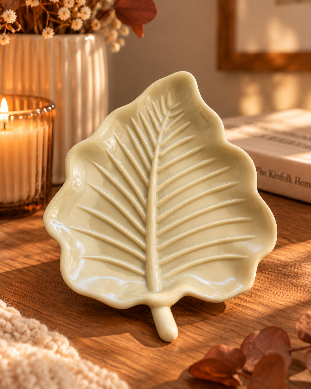 Vide-poche Leaf Touch en forme de feuille beige brillante, posé sur une table en bois dans une ambiance automnale chaleureuse, entouré de fleurs séchées et d'une bougie.
